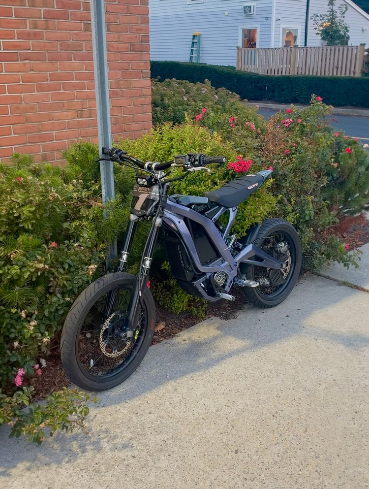 Purple Surron Light Bee X supermoto build parked by a hedge